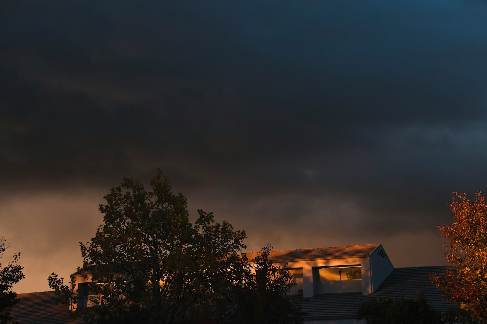A cloudy sky with a building and trees in the foreground